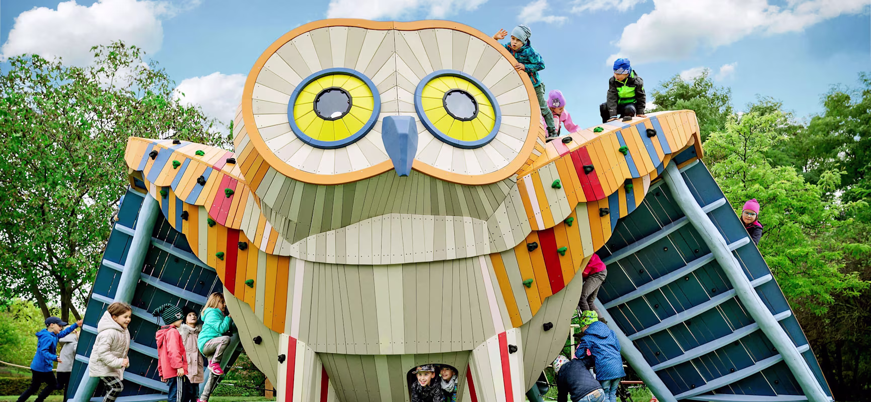 Children playing on a wooden owl playground sculpture in Prague