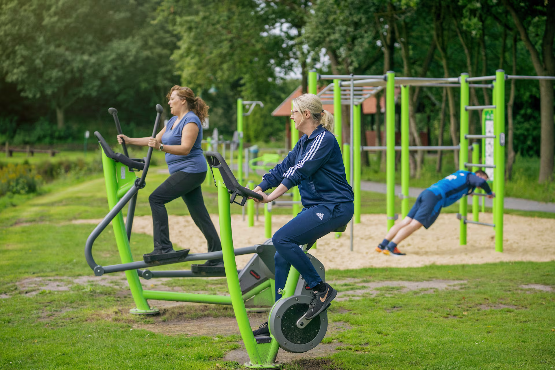 drei Männer machen Liegestütze an einem Holz Fitnessgerät im Freien