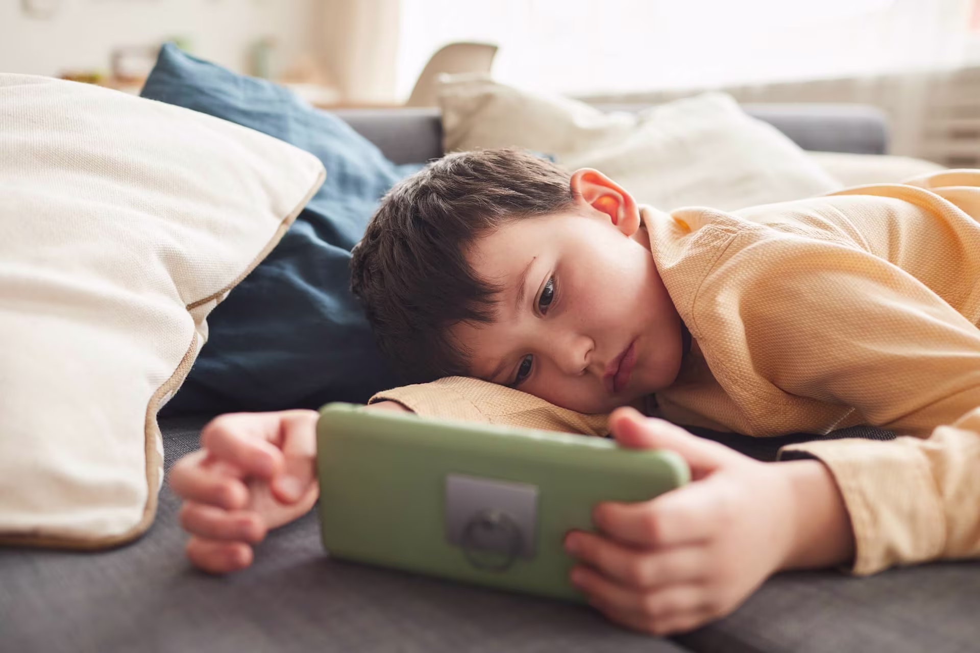 a young boy laying on a couch with a tablet.