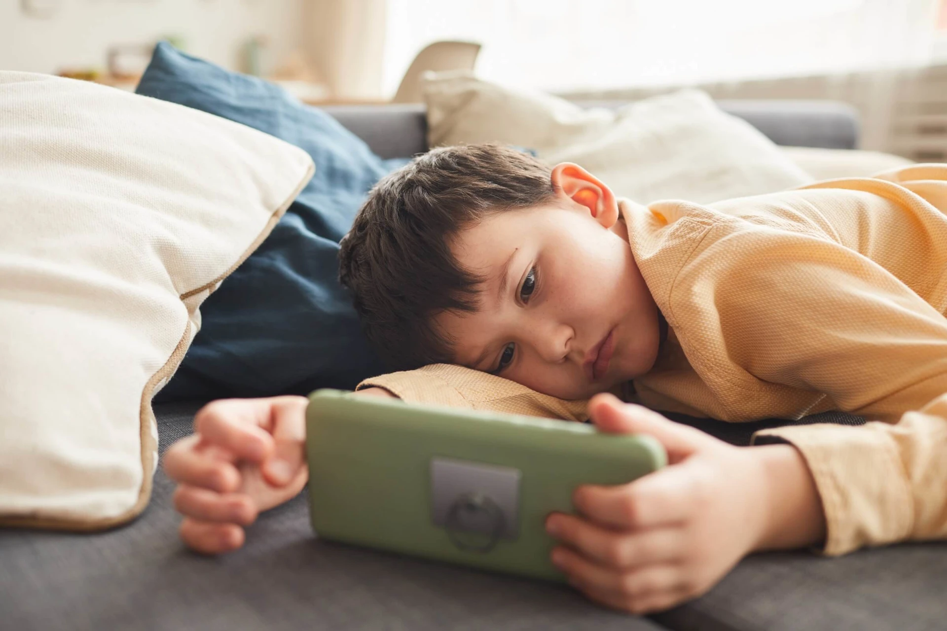 a young boy laying on a couch with a tablet.
