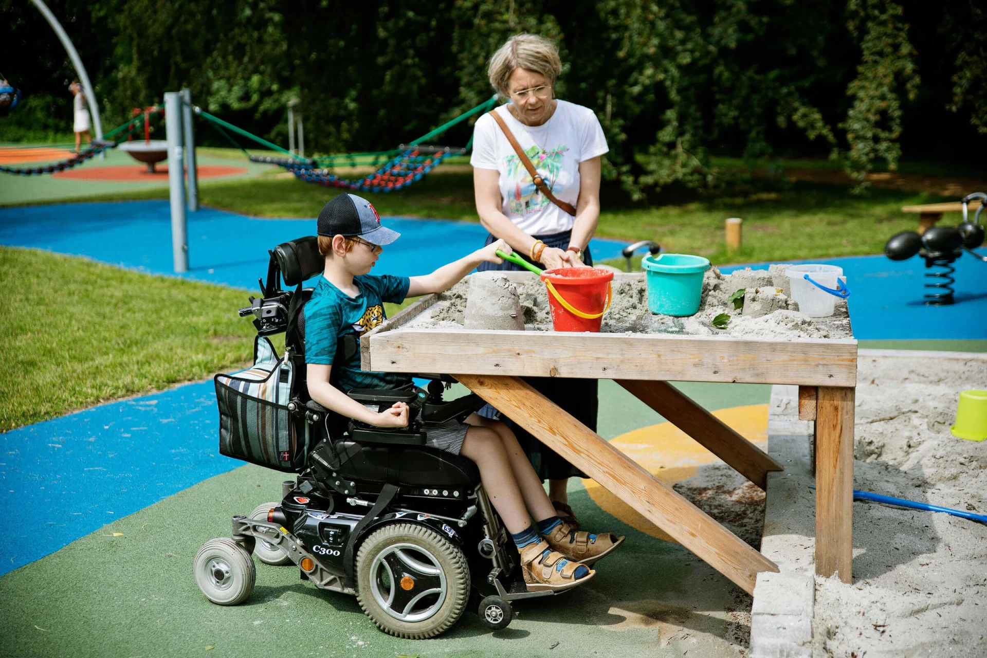 pyörätuolia käyttävä poika leikkimässä korotetulla hiekkapöydällä leikkipuistossa