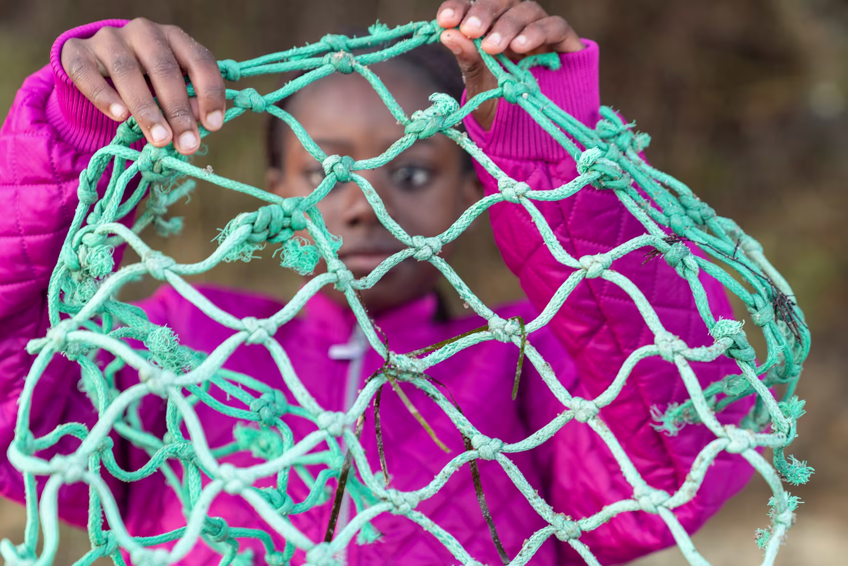 girl holding up fishing nets found on the beach