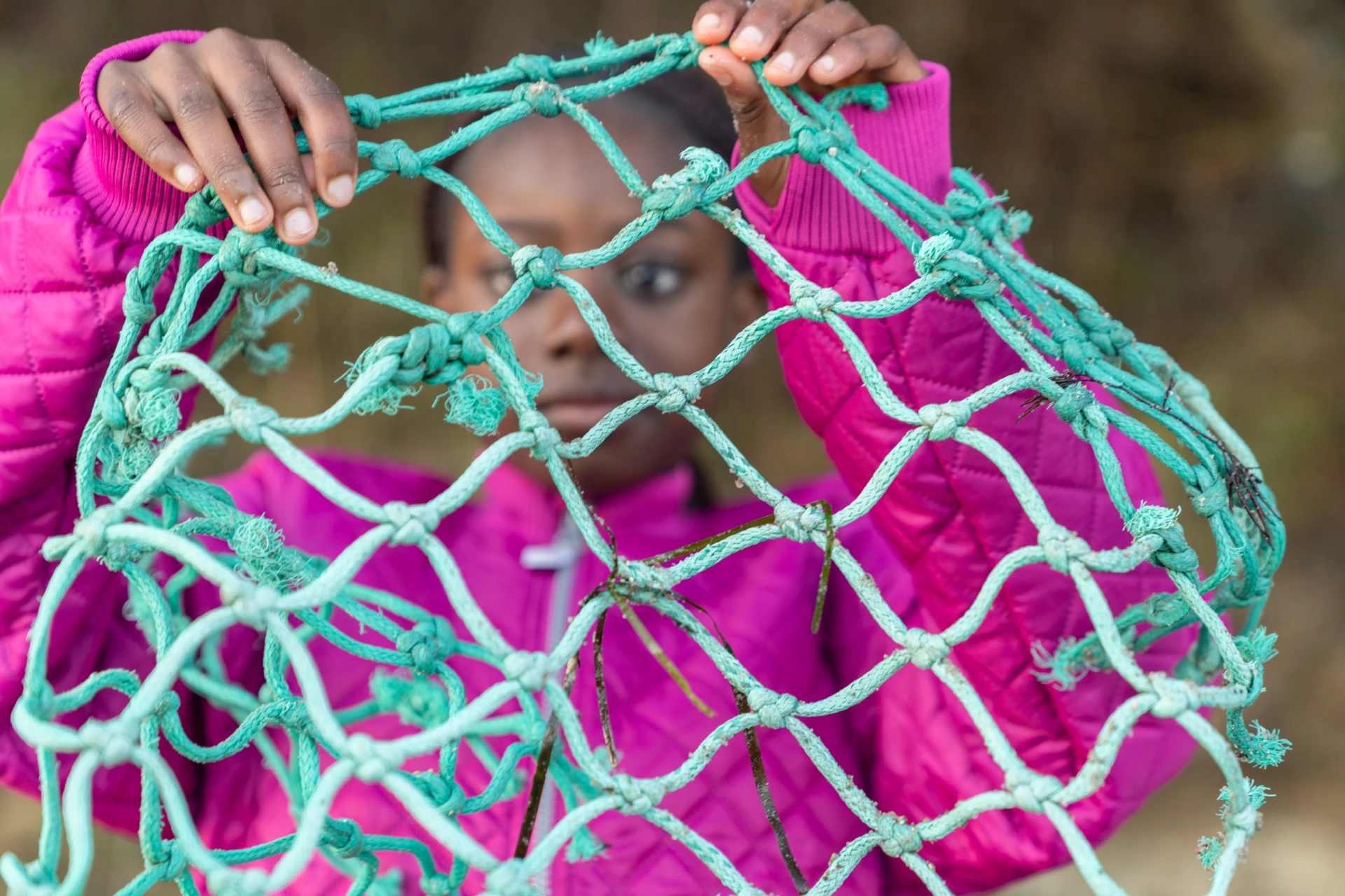 tyttö pitelee rannalta löytyneitä kalaverkkoja käsissään