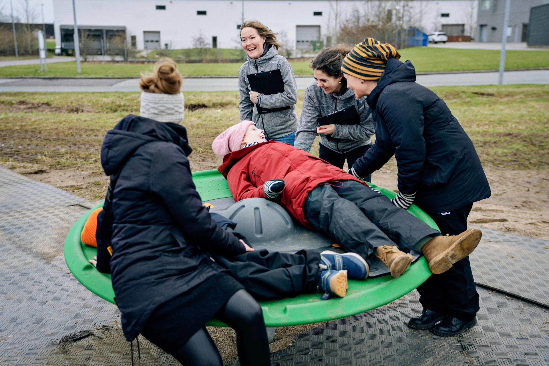 a group of people standing around a children laying on top of a inclusive play equipment