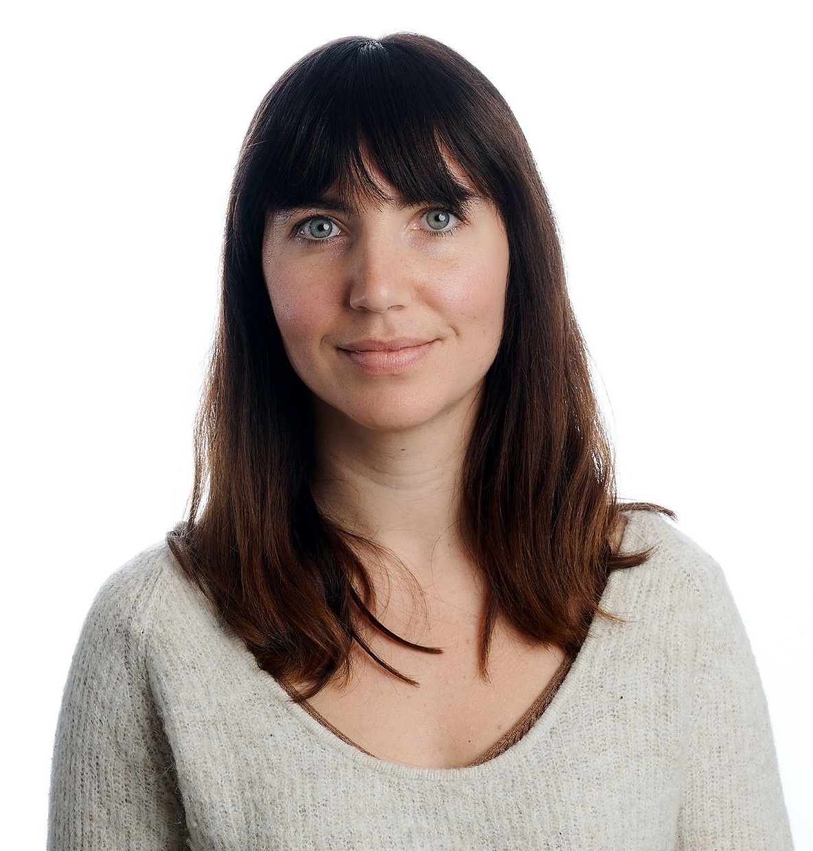 Person with long brown hair in a light knit sweater, facing forward against a plain white background, face blurred for privacy