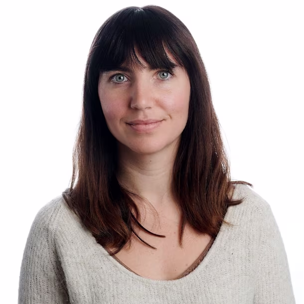 Person with long brown hair in a light knit sweater, facing forward against a plain white background, face blurred for privacy