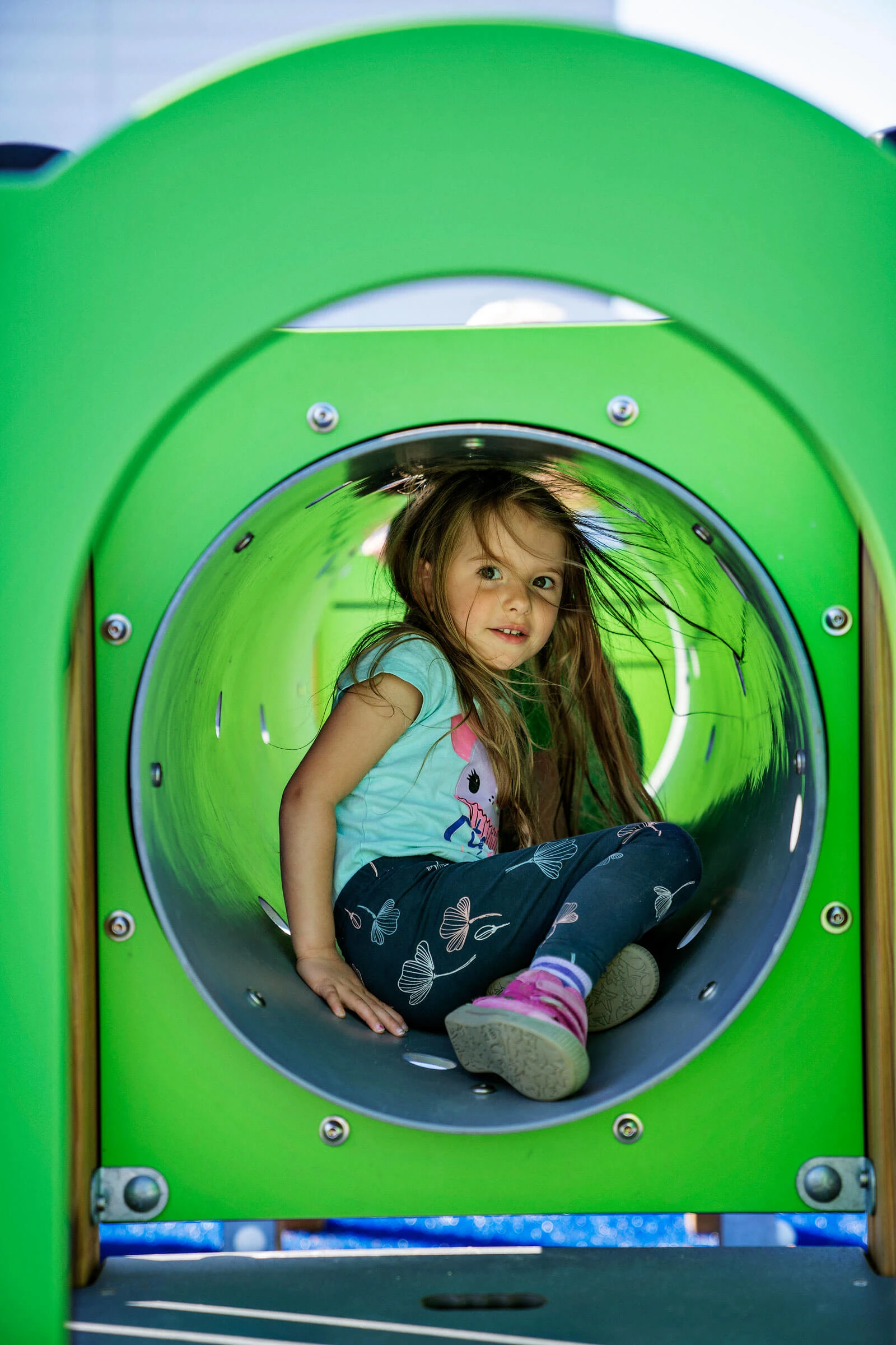 school girl sitting in a tube on a play structure for primary schools