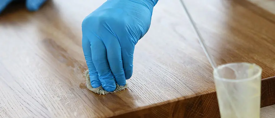 Een hand met handschoen maakt een stuk hout schoon | Une main gantée nettoie un morceau de bois