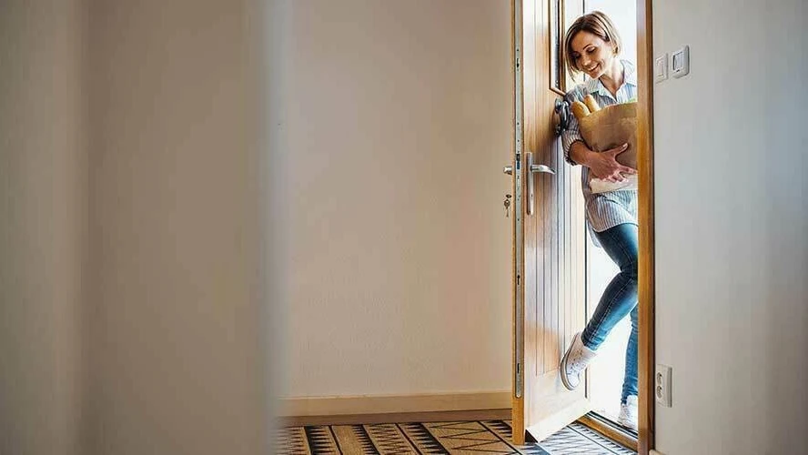 Een vrouw komt met een tas boodschappen via de voordeur naar binnen | Une femme entre par la porte d'entrée avec un sac de provisions