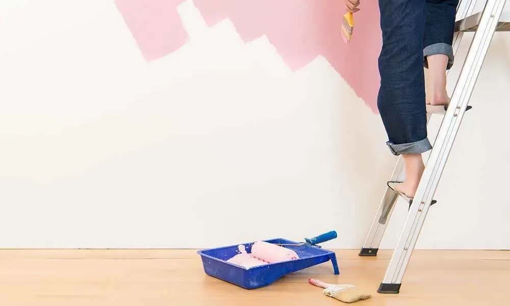 Vrouw staat op ladder voor geverfde muur | Femme debout sur une échelle devant un mur peint