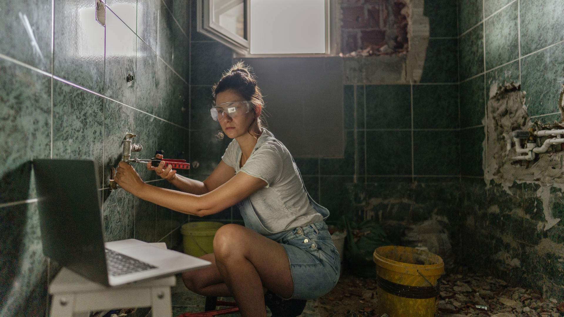 Vrouw repareert sanitair in een badkamer met online instructies. | Femme répare la plomberie dans la salle de bain à l'aide d'instructions en ligne.