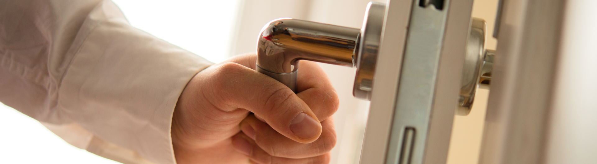 Hand die een deurkruk vastpakt om een deur te openen. | Main tenant une poignée de porte pour ouvrir une porte.