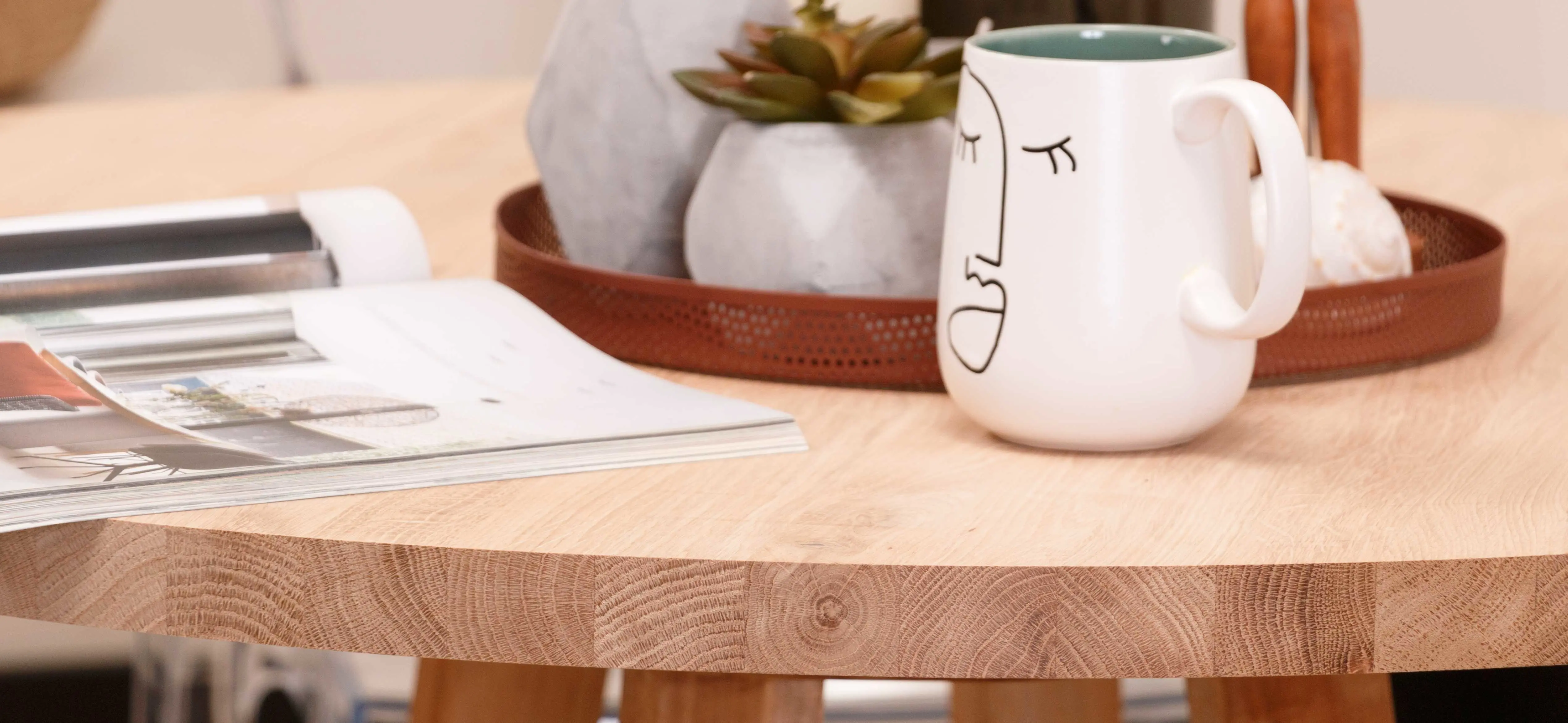 Detail van een tafelblad met doorlopende eikenhouten latten, tijdschrift en mok, decoratief dienblad met planten. | Détail d'un plateau de table en lattes continues de chêne, avec magazine et tasse, plateau décoratif avec plantes.