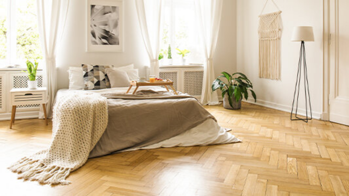 Een bed in een slaapkamer met beige muren en houten vloer | Un lit dans une chambre aux murs beiges et au sol en bois