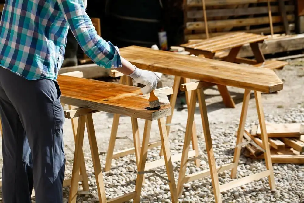 Een man beitst het hout op een standaard | Un homme teinte le bois d'un stand