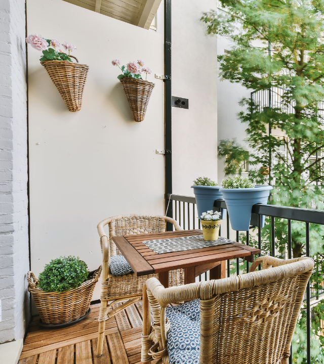 Een gezellig balkom met een rieten bistroset, kussens, en enkele plantjes | Un balcon confortable avec tables et chaises bistro en osier, des coussins et quelques plantes