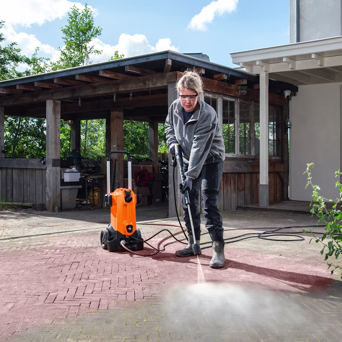 Een vrouw reinigt een terras met een hogedrukreiniger | Une femme nettoie une terrasse avec un nettoyeur haute pression