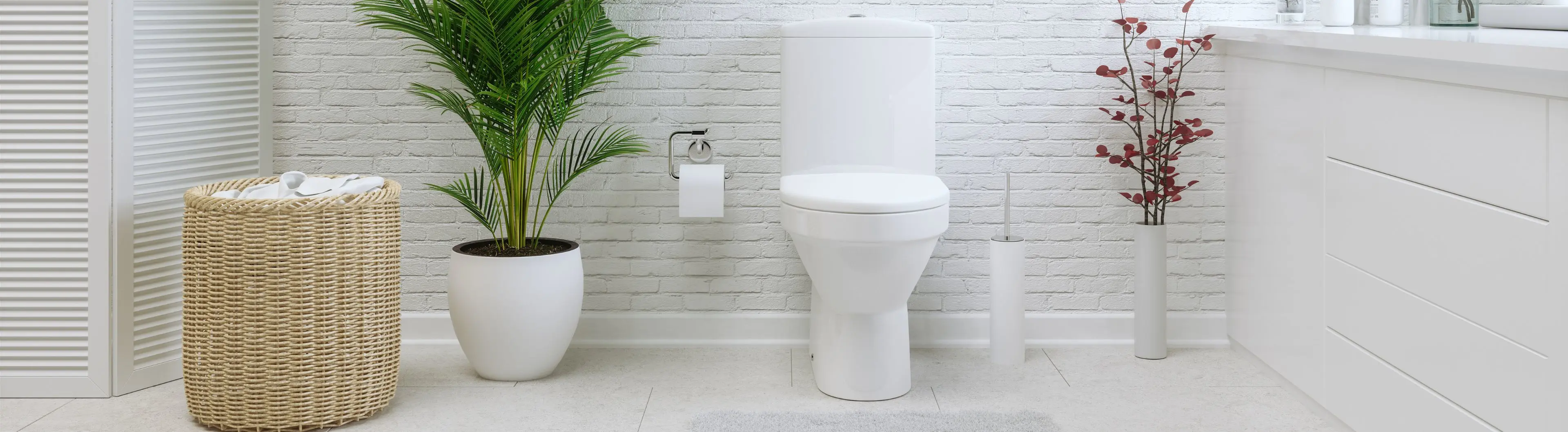 Moderne badkamer met toilet, witte kast, rieten wasmand en planten voor een frisse uitstraling. | Salle de bain moderne avec toilettes, meuble blanc, panier à linge en osier et plantes pour une touche de fraîcheur.