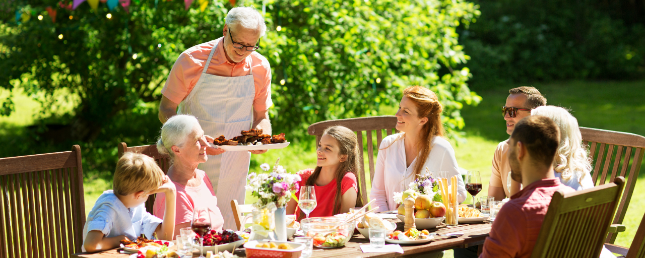 een familie die buiten rond een tafel met eten zit | une famille assise à l'extérieur autour d'une table avec de la nourriture