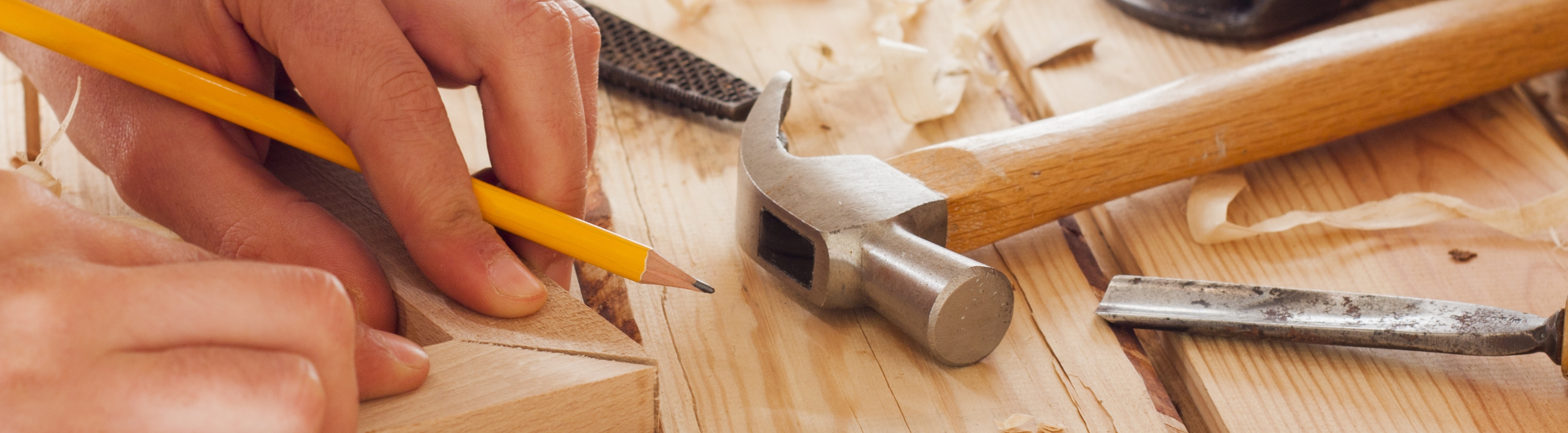 Hand markeert hout met potlood, omringd door hamer en beitel op werkbank | Main marque le bois avec un crayon, entourée d'un marteau et d'un ciseau sur l'établi