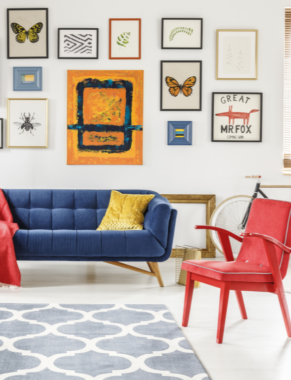 Een kleurrijke living met blauwe sofa, rode stoel en verschillende schilderijen en posters aan de muur | Un salon coloré avec un canapé bleu, une chaise rouge et divers tableaux et affiches au mur