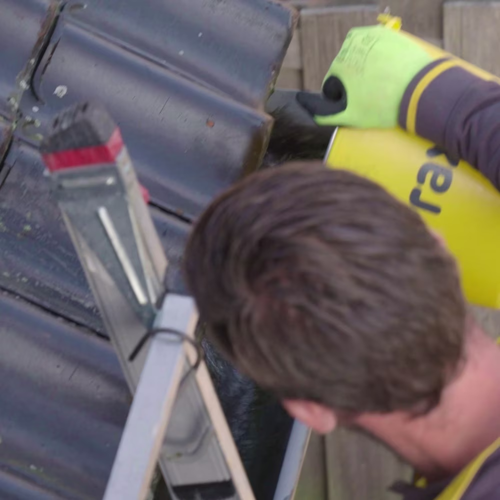 man met bruin haar staat op een ladder en maakt een dakgoot schoon met een gele emmer - praxis pagina voorbereiden op storm