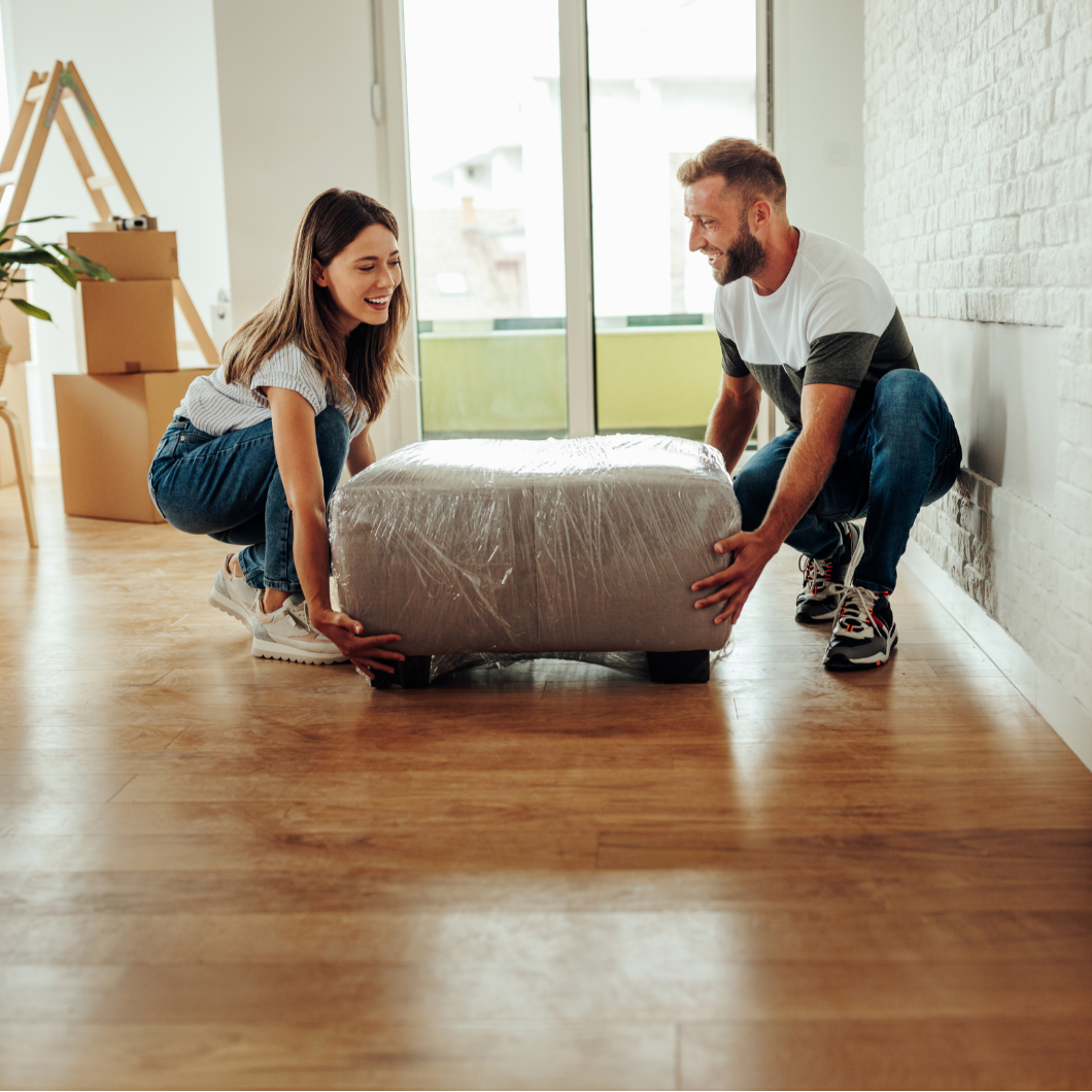 Twee mensen tillen een ingepakte fauteuil tijdens een verhuizing in een kamer met dozen | Deux personnes soulèvent un fauteuil emballé lors d’un déménagement dans une pièce avec des cartons