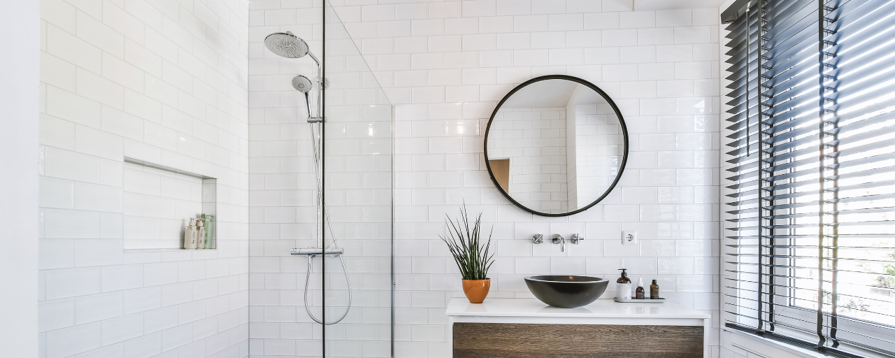 Een moderne badkamer met witte tegels, inloopdouche en ronde spiegel boven de houten wastafel | Une salle de bains moderne avec des carreaux blancs, une douche à l'italienne et un miroir rond au-dessus du lavabo en bois