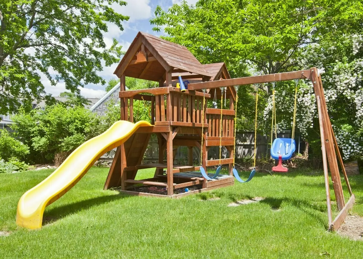 Een houten speelhuisje met schommels en een glijbaan | Une maison de jeux en bois avec des balançoires et un toboggan