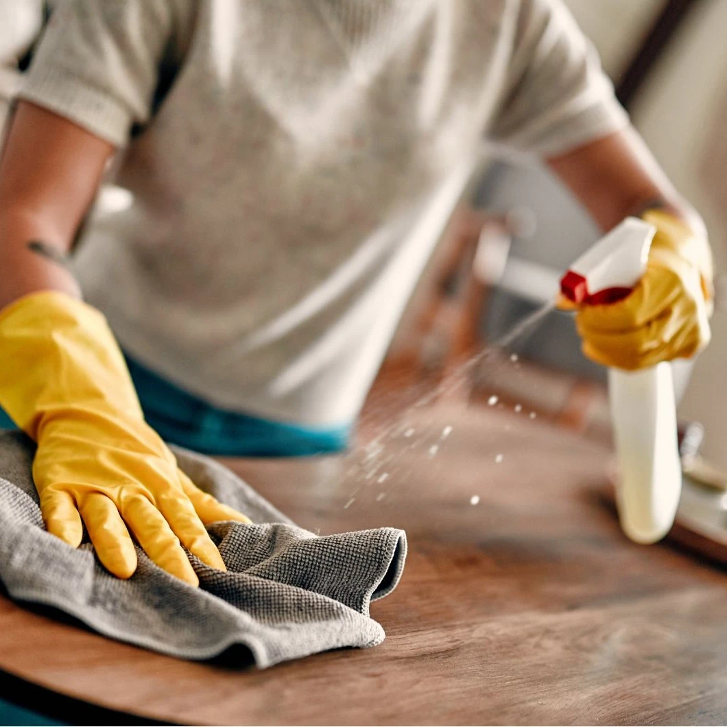 Hand met gele handschoen reinigt houten oppervlak met doek en reinigingsspray | Main avec un gant jaune nettoie une surface en bois avec un chiffon et un spray nettoyant