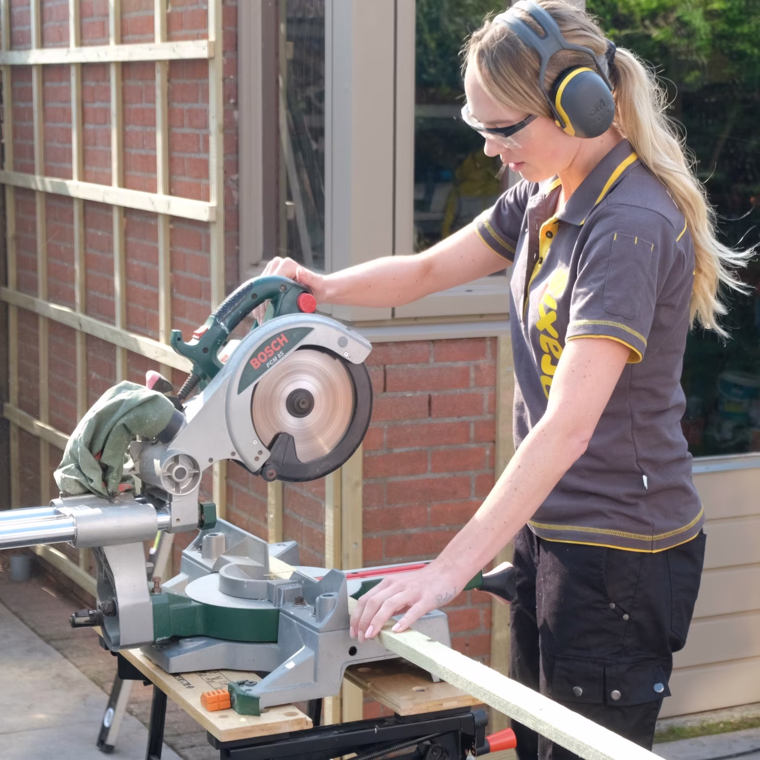 Vrouw met lang blond haar zaagt een lattenwand op maat: praxis blog lattenwanden trends 2026