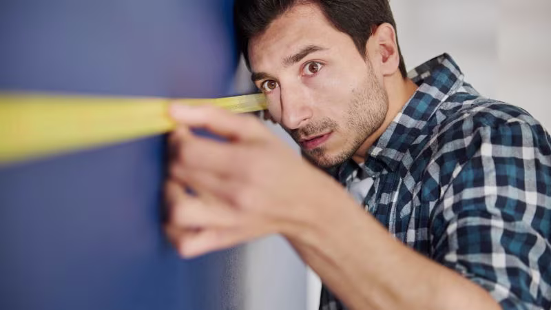 Man in geruite hemd meet nauwkeurig een muur met een rolmaat | Homme en chemise à carreaux mesurant un mur avec précision à l'aide d'un mètre ruban