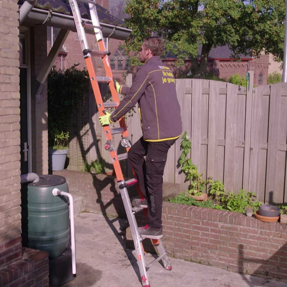 man in grijze jas klimt op ladder naar de dakgoot van een huis om die te gaan schoonmaken - praxis pagina voorbereiden op storm