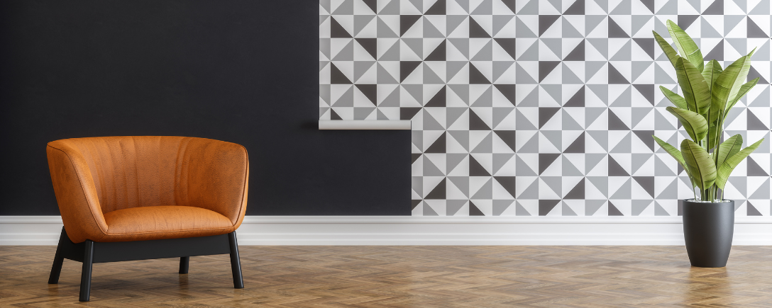 Een oranje stoel voor een muur met een geometrisch patroon en een plant aan de rechterkant | Une chaise orange devant un mur à motifs géométriques et une plante à droite.