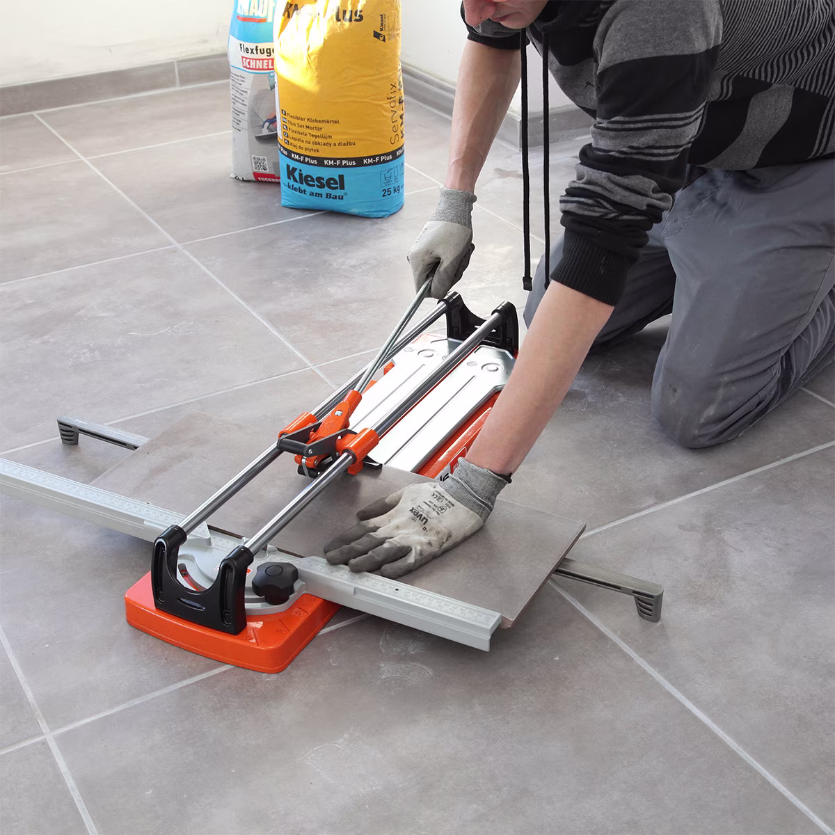 Een man snijdt een tegel met een tegelsnijder | Un homme coupe un carreau avec un coupe-carreaux.