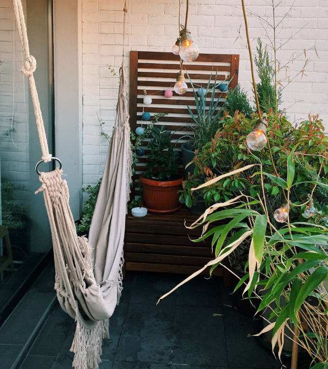 Een klein balkon met een witte hangmat, lichtjes, en verschillende planten | Un petit balcon avec un hamac blanc, des lumières et diverses plantes