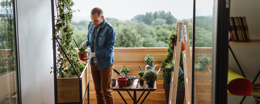 Een man staat op zijn balkon zijn planten te verzorgen | Un homme se tient sur son balcon et s'occupe de ses plantes