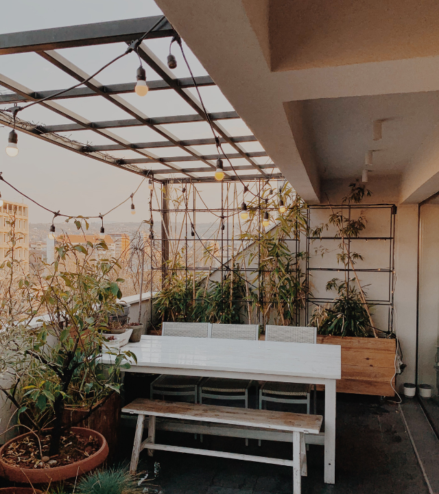 Een gezellig balkon met een witte eettafel, planten en lichtslingers | Un balcon accueillant avec une table à manger blanche, des plantes et des guirlandes lumineuses 