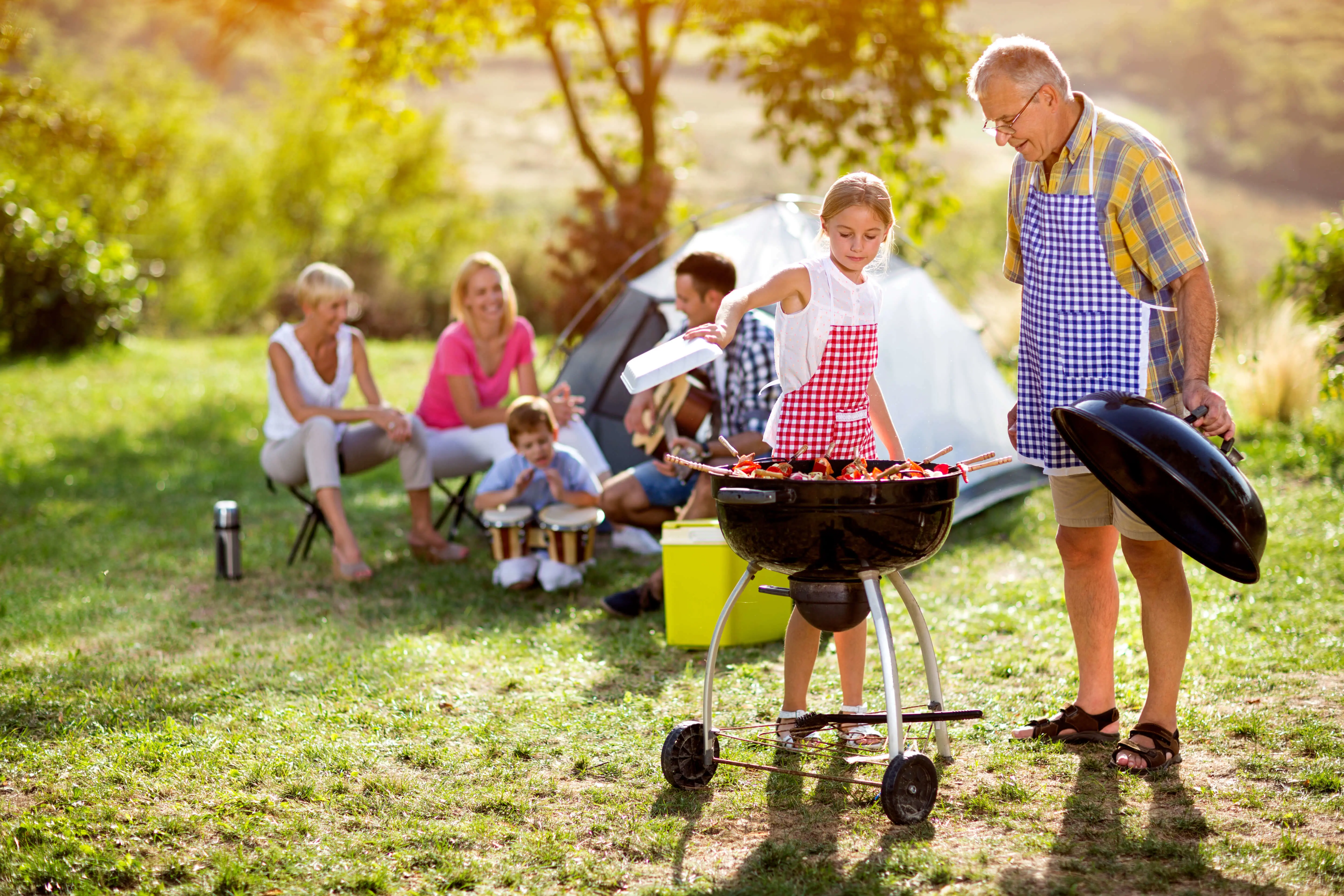 Een meisje staat achter de barbecue en een man houdt de deksel vast | Une fille se tient derrière le barbecue et un homme tient le couvercle