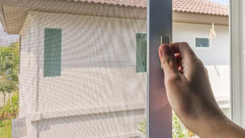 een persoon opent een vensterscherm met een huis op de achtergrond | une personne ouvre la moustiquaire d'une fenêtre avec une maison en arrière-plan