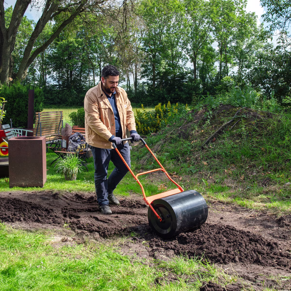 Een man egaliseert de aarde met een tuinwals | Un homme égalise la terre avec un rouleau à gazon