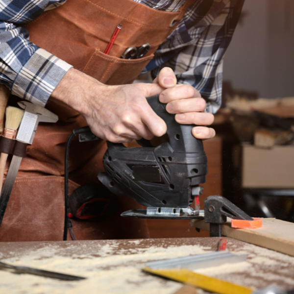 Een man snijdt door een stuk hout met een decoupeerzaag in zijn atelier | Un homme découpe un morceau de bois à l'aide d'une scie sauteuse dans son atelier