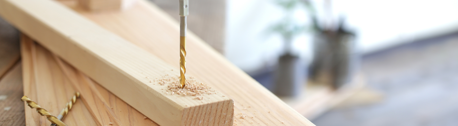 Boormachine die een gat in een houten plank boort, met houtspaanders. | Perceuse perçant un trou dans une planche en bois, avec des copeaux de bois.