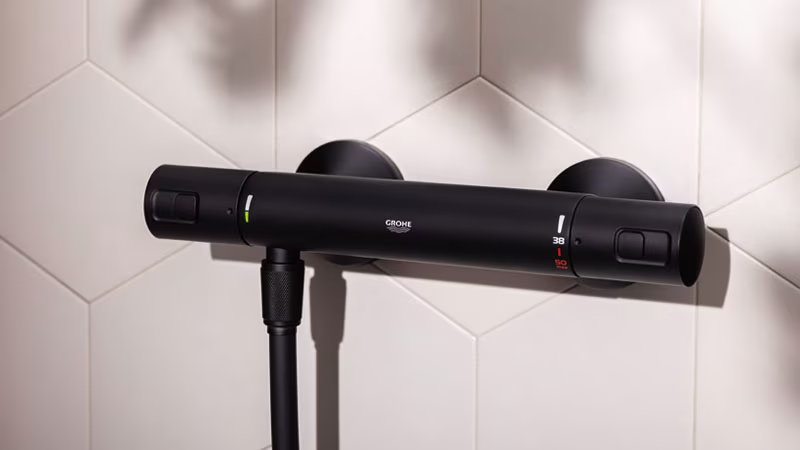Een zwarte douchethermostaat op een lichte betegelde muur | Un mitigeur thermostatique de douche noir sur un mur carrelé clair