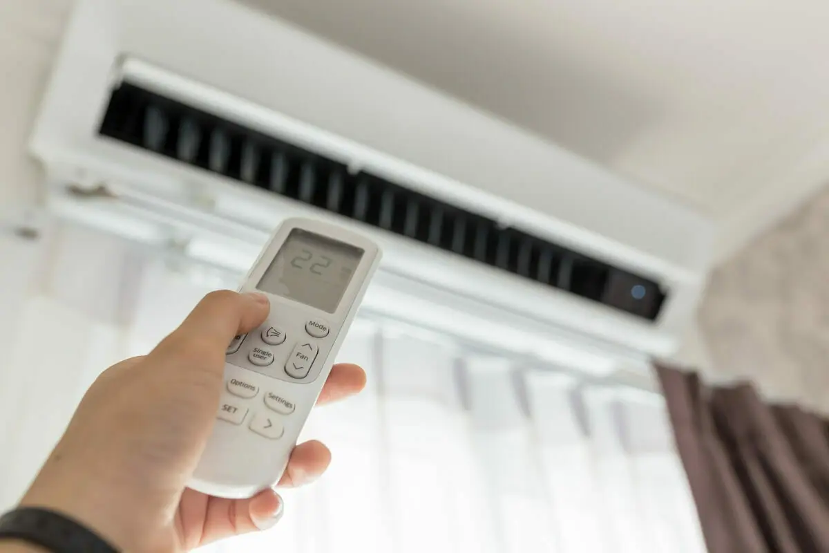 Een hand houdt een afstandsbediening vast en richt deze op de airco | Une main tient une télécommande et la dirige vers le climatiseur