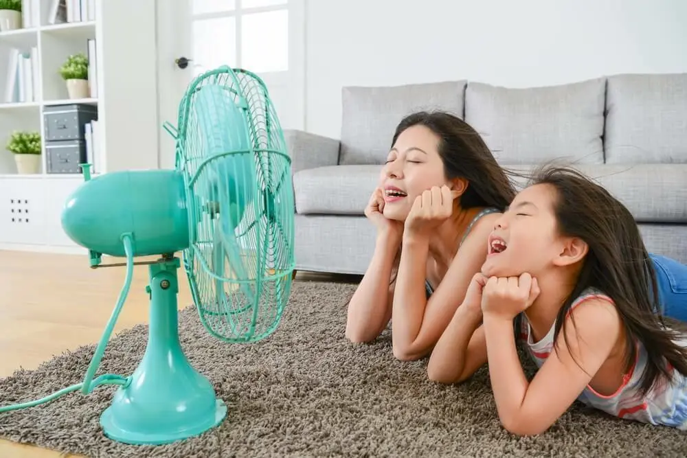 Twee mensen liggen op de grond voor een ventilator | Deux personnes allongées sur le sol devant un ventilateur