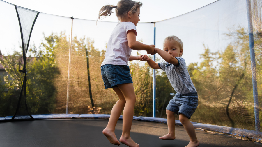 Twee kindjes springen op een trampoline in de tuin | Deux enfants sautant sur un trampoline dans le jardin