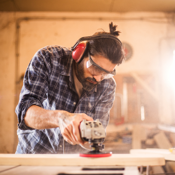 een man gebruikt een cirkelvormige schuurmachine op een stuk hout | un homme utilise une ponceuse circulaire sur une pièce de bois