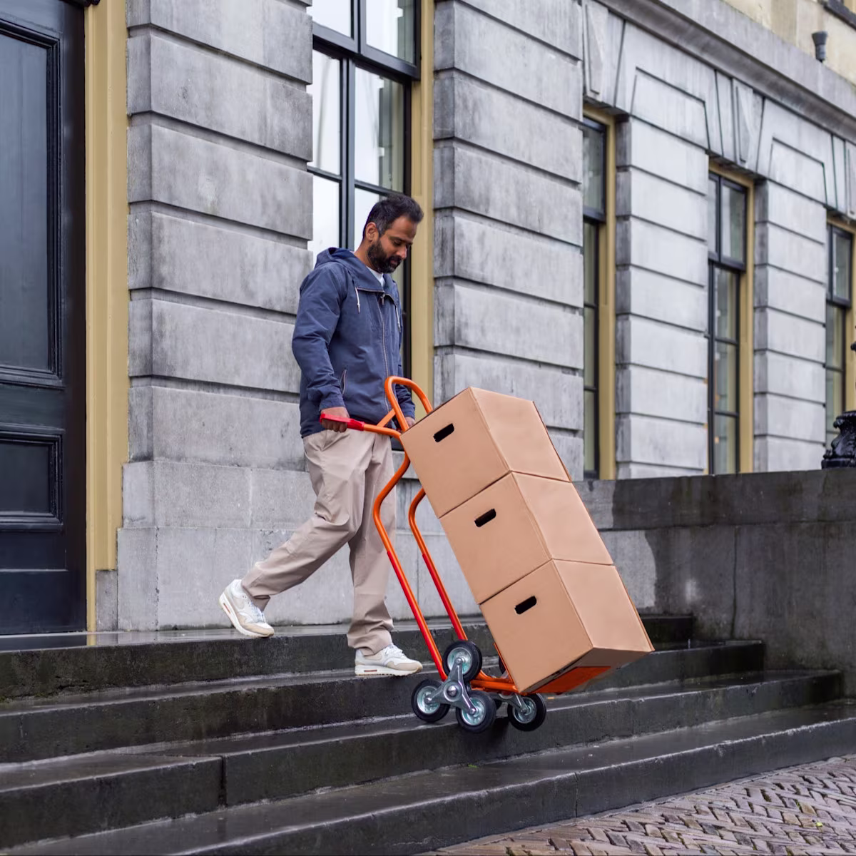 Een man rijdt dozen van een trap met een steekwagen | Un homme descend des boîtes avec un diable