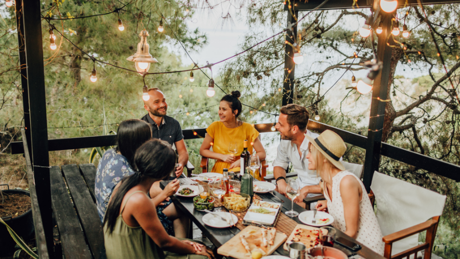 Vrienden genieten samen van een maaltijd buiten op een terras versierd met verschillende sfeerlichtjes | Des amis prennent un repas ensemble à l'extérieur sur une terrasse décorée de diverses lumières d'ambiance